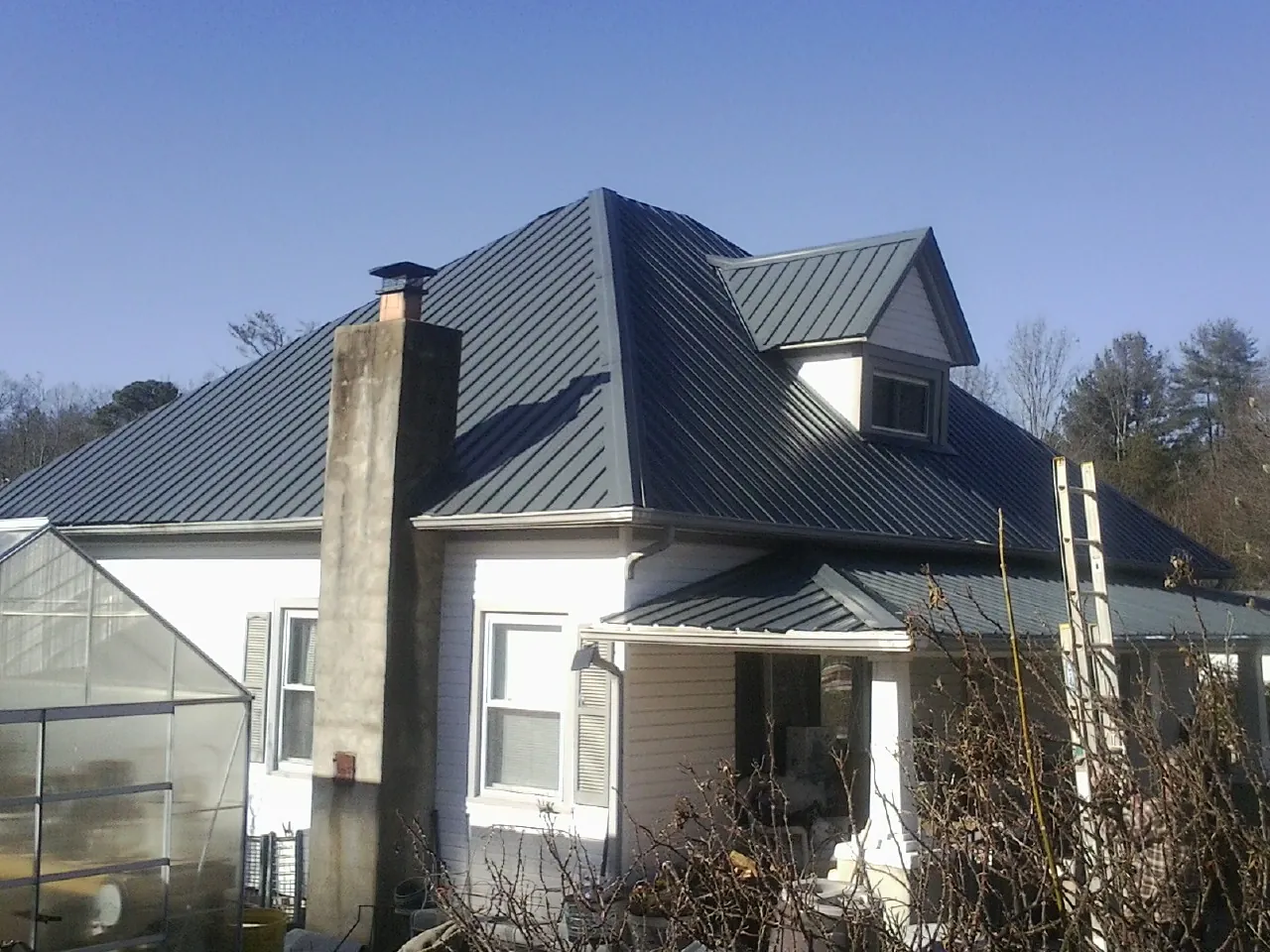 Dark blue standing seam metal roof on a white farmhouse with dormer — Slate & Tile Roof Repair by Roofing Brothers in Leland