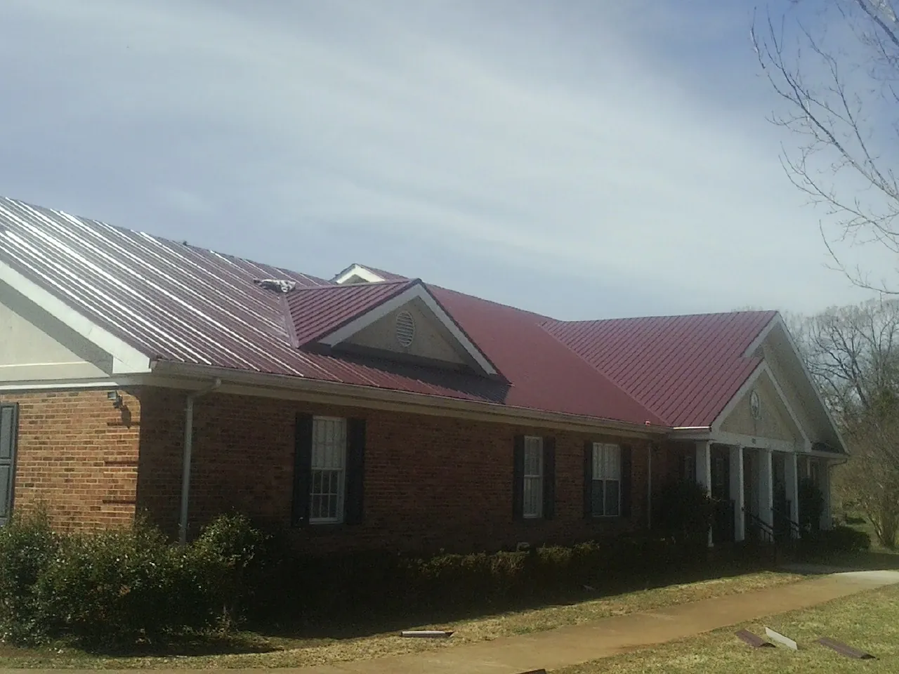 Red metal roof with gabled entries on a long brick building, from a Hail Damage Roof Repair job in Leland
