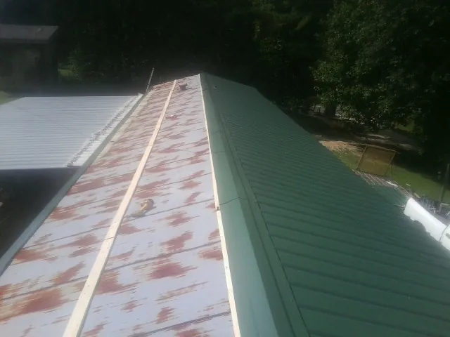 Old rusted panels beside newly installed green metal roofing — Wind Damage Roof Repair by Roofing Brothers in Leland
