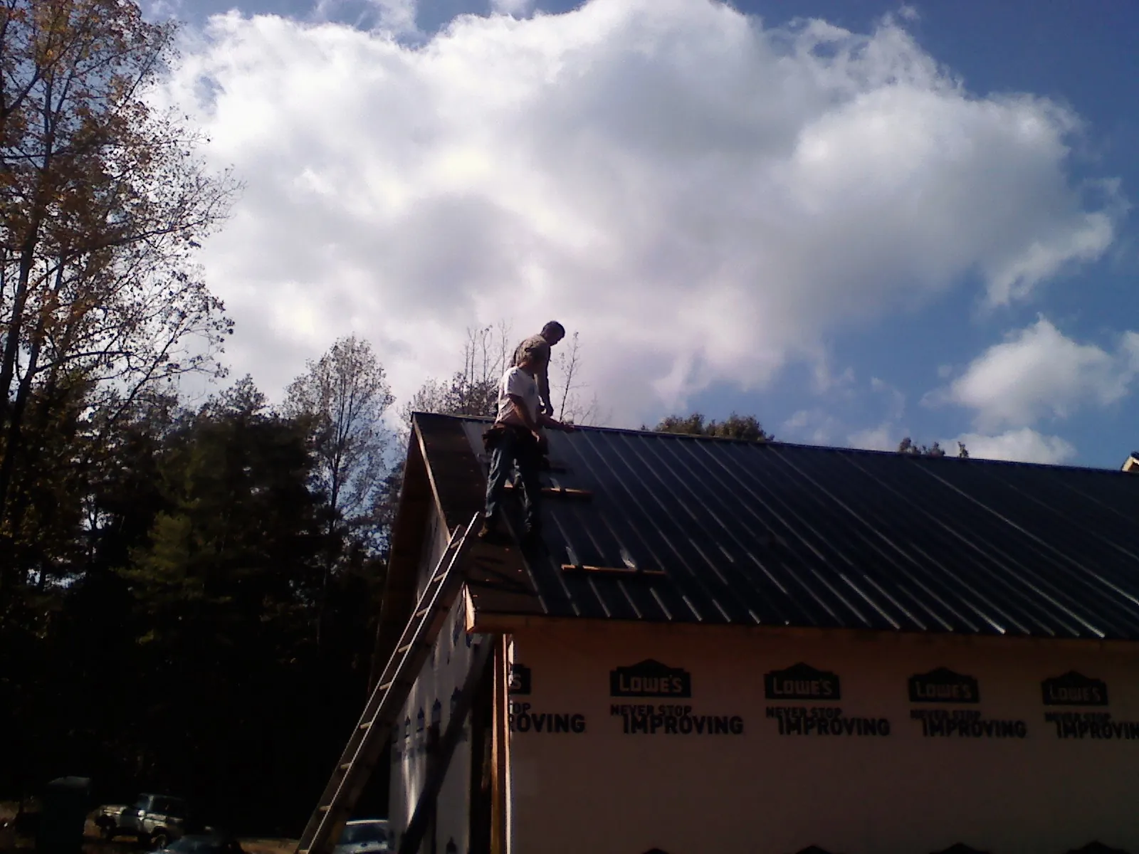 Roofer fastening dark metal panels high against a cloudy sky, from a Roof Inspection job in Leland