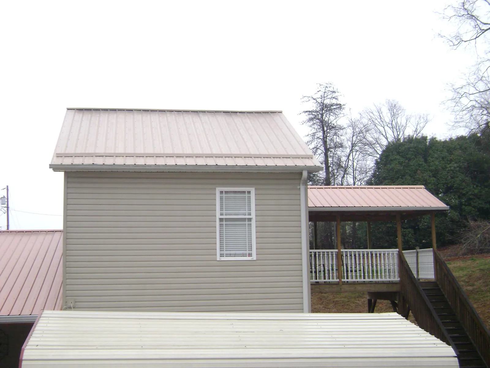 Tan metal roofs on a two story addition and attached porch, from a Roof Replacement job in Leland